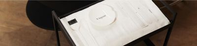 A white Kerastase bowl with a small spatula and a brush on a white cloth background.