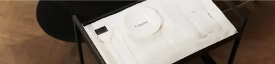 A white Kerastase bowl with a small spatula and a brush on a white cloth background.
