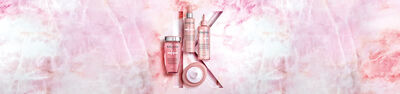 A collection of beauty products displayed on a pink marble background, featuring various bottles and jars arranged artistically.