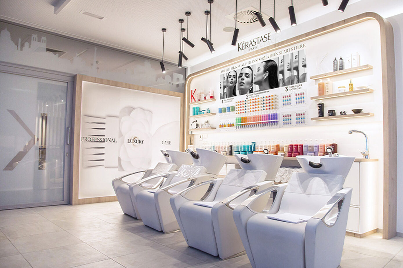 A modern salon interior featuring sleek white styling chairs and a display shelf of colorful hair care products illuminated by soft lighting.