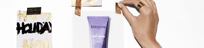 A hand showcasing a tube of Kerastase hair care product, positioned among holiday-themed decorations and text on a white background.