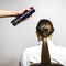 A hand holding a spray can is about to apply hair products to the back of a woman’s long, sleek hairstyle. She is seated and facing away from the camera.