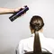 A hand holding a spray can is about to apply hair products to the back of a woman’s long, sleek hairstyle. She is seated and facing away from the camera.