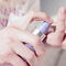 A hand holding a purple pump bottle, dispensing a cream onto a fingertip.