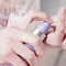 A hand holding a purple pump bottle, dispensing a cream onto a fingertip.