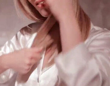 A person wearing a white satin shirt is gently styling their long hair.