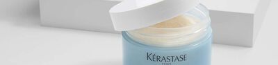 A close-up image of a Kerastase Paris hair product jar with the lid slightly open, revealing a creamy texture inside.