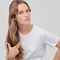 A young woman with long, wavy hair wearing a plain white t-shirt, looking thoughtfully at the camera with a slight expression.