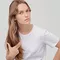 A young woman with long, wavy hair wearing a plain white t-shirt, looking thoughtfully at the camera with a slight expression.