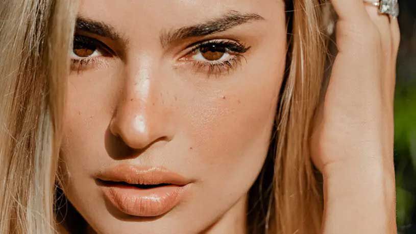 Close-up of a woman with light blonde hair, striking features, and a natural makeup look, looking directly at the camera.