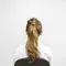 A woman with long, wavy hair is seated, facing away from the camera against a plain white wall. She is wearing a white shirt.