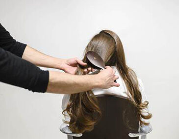 A person is brushing long hair of another person, who is seated and facing away.