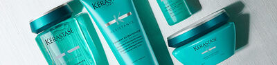 A close-up image of Kerastase hair care products, featuring two turquoise bottles labeled "Resistance" and "Fondant Extentioniste."