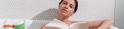 A woman gazes thoughtfully at the camera while holding an open book. She has a natural look and is surrounded by a light, textured background.