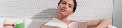 A woman gazes thoughtfully at the camera while holding an open book. She has a natural look and is surrounded by a light, textured background.