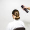 A person sitting in a chair with a sleek bun hairstyle is having hair spray applied from behind.