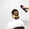 A person sitting in a chair with a sleek bun hairstyle is having hair spray applied from behind.