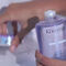 A close-up of a person's hand holding a bottle of Kerastase shampoo, with another product visible in the background.