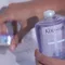 A close-up of a person's hand holding a bottle of Kerastase shampoo, with another product visible in the background.