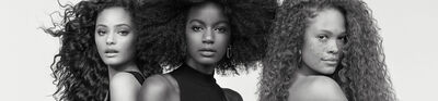 A black and white portrait of two women standing back to back, showcasing different hairstyles—one with wavy hair and the other with voluminous curls. Both have natural makeup, highlighting their features.