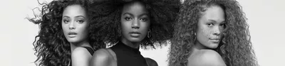 A black and white portrait of two women standing back to back, showcasing different hairstyles—one with wavy hair and the other with voluminous curls. Both have natural makeup, highlighting their features.