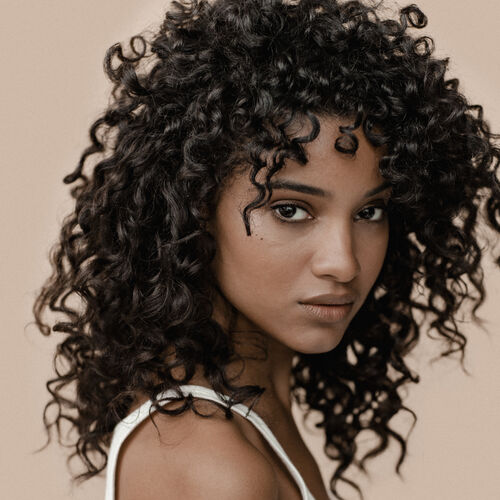 A close-up portrait of a woman with curly hair, displaying a confident expression against a neutral background.