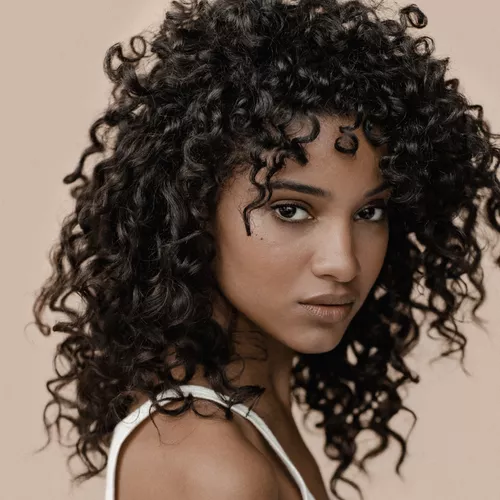 A close-up portrait of a woman with curly hair, displaying a confident expression against a neutral background.