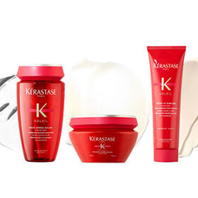 Three Kerastase hair care products are displayed against a light background. The products include a shampoo, a hair mask, and a leave-in treatment, all in vibrant red packaging.