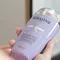 A person holding a bottle of Kerastase purple shampoo with a sleek design and holographic label.