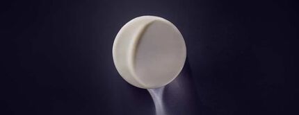 A minimalist, round, white pill rests on a dark surface, casting a soft shadow.