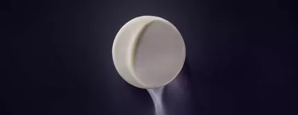 A minimalist, round, white pill rests on a dark surface, casting a soft shadow.