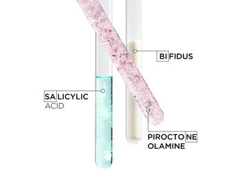 Three test tubes filled with different substances: one contains a pink crystalline solid labeled "Salicylic Acid," the second has a blue liquid labeled "Bifidus," and the third contains a white powder labeled "Piroctone Olamine."