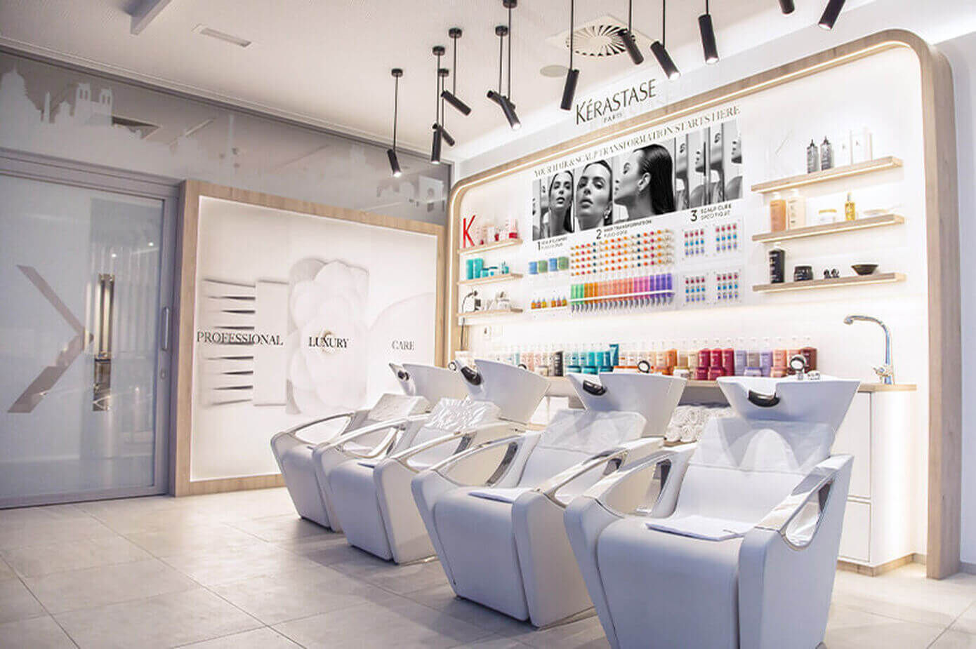 A modern salon interior featuring three stylish shampoo chairs, a well-organized shelves displaying various hair products, and a bright, minimalist design.