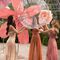 Three women in a greenhouse are joyfully interacting with a large, translucent, bubble-like structure, surrounded by vibrant flower decorations.