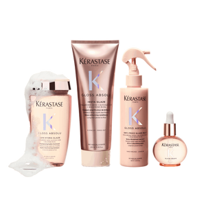 A collection of four Kerastase hair products, including a shampoo, a treatment, a spray, and a serum, all featuring elegant rose gold packaging. The products are displayed with a bubbly foam effect, suggesting a hair care routine focused on glossy and shiny results.