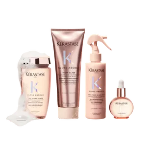 A collection of four Kerastase hair products, including a shampoo, a treatment, a spray, and a serum, all featuring elegant rose gold packaging. The products are displayed with a bubbly foam effect, suggesting a hair care routine focused on glossy and shiny results.