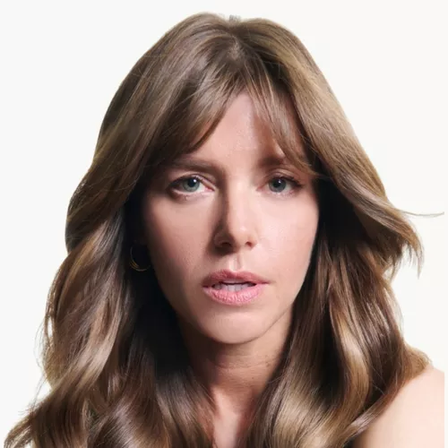  An older woman with bouncy dark blonde hair on a light grey background​