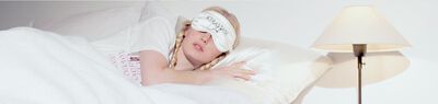 A person with braided blonde hair is lying on a pillow, wearing a satin sleep mask, suggesting a peaceful sleep or rest.