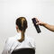 A person with their back to the camera is sitting in a chair while another person is holding a can of hair spray above their head, preparing to style their hair.
