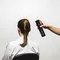 A person with their back to the camera is sitting in a chair while another person is holding a can of hair spray above their head, preparing to style their hair.
