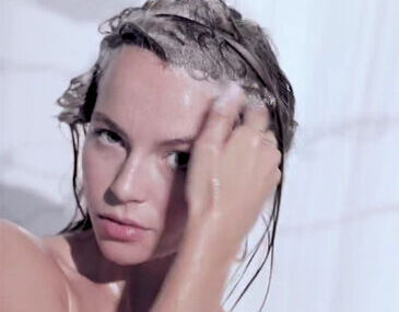 A person with wet hair is applying shampoo while looking directly at the camera. Water is dripping down their face and shoulders.
