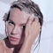 A person with wet hair is applying shampoo while looking directly at the camera. Water is dripping down their face and shoulders.