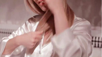 A person wearing a white satin shirt is gently styling their long hair.