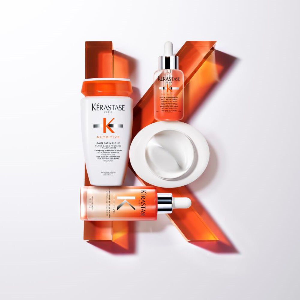 A flat lay of Kerastase hair care products, including a shampoo, serum, and mask, arranged with vibrant orange accents.