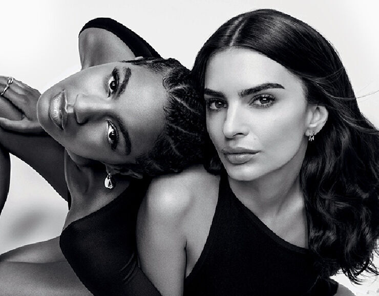 Two women pose closely together against a light background, showcasing different hairstyles and wearing black outfits. Their expressions are confident and engaging.