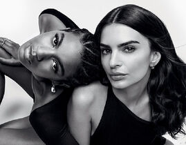 Two women pose closely together against a light background, showcasing different hairstyles and wearing black outfits. Their expressions are confident and engaging.