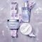 Three Kerastase hair care products arranged on a reflective surface, surrounded by shimmering crystal-like pieces. The items include a jar, a bottle, and a pouch, all featuring soft, pastel colors.