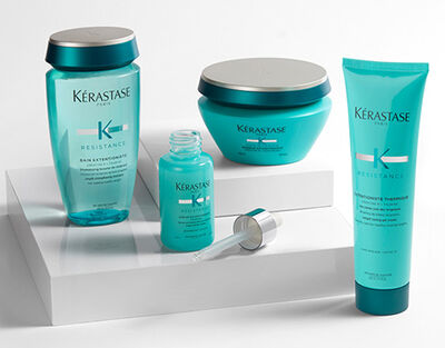 A flat lay of Kerastase hair care products, including a shampoo, conditioner, serum, and treatment, arranged on a textured surface with a ruler marking in the background.