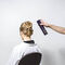 A person with an elegant updo hairstyle sits in a salon chair, while another hand holds a can of hair spray, ready to apply it.