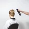 A person with an elegant updo hairstyle sits in a salon chair, while another hand holds a can of hair spray, ready to apply it.